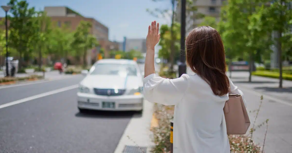 Woman hailing a Taxi Den Haag cab on a sunny street in The Hague.